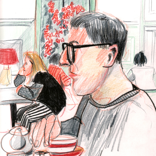 A sketch of a man with glasses sitting at a table in a cafe. He holds a teacup, with a teapot and milk jug nearby. In the background, a woman with striped pants sits at another table near a red lamp and red flower decorations.